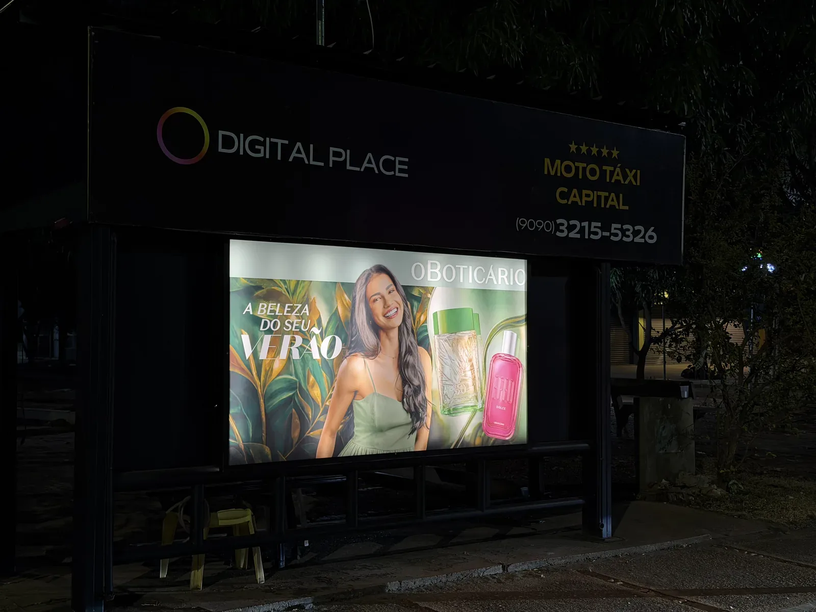 Painel backlight da Digital Place aceso à noite em abrigo de mototáxi na Avenida JK, em Palmas, com campanha de verão do O Boticário