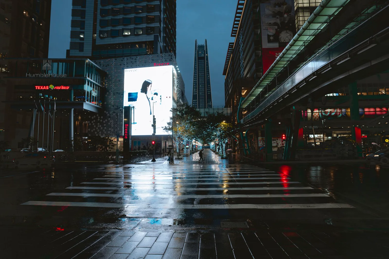 Rua molhada à noite em Taipei, com uma tela digital acesa refletida na calçada