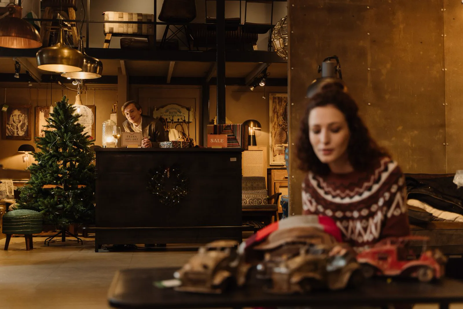 Loja decorada para o Natal com o lojista no balcão e uma cliente escolhendo presentes