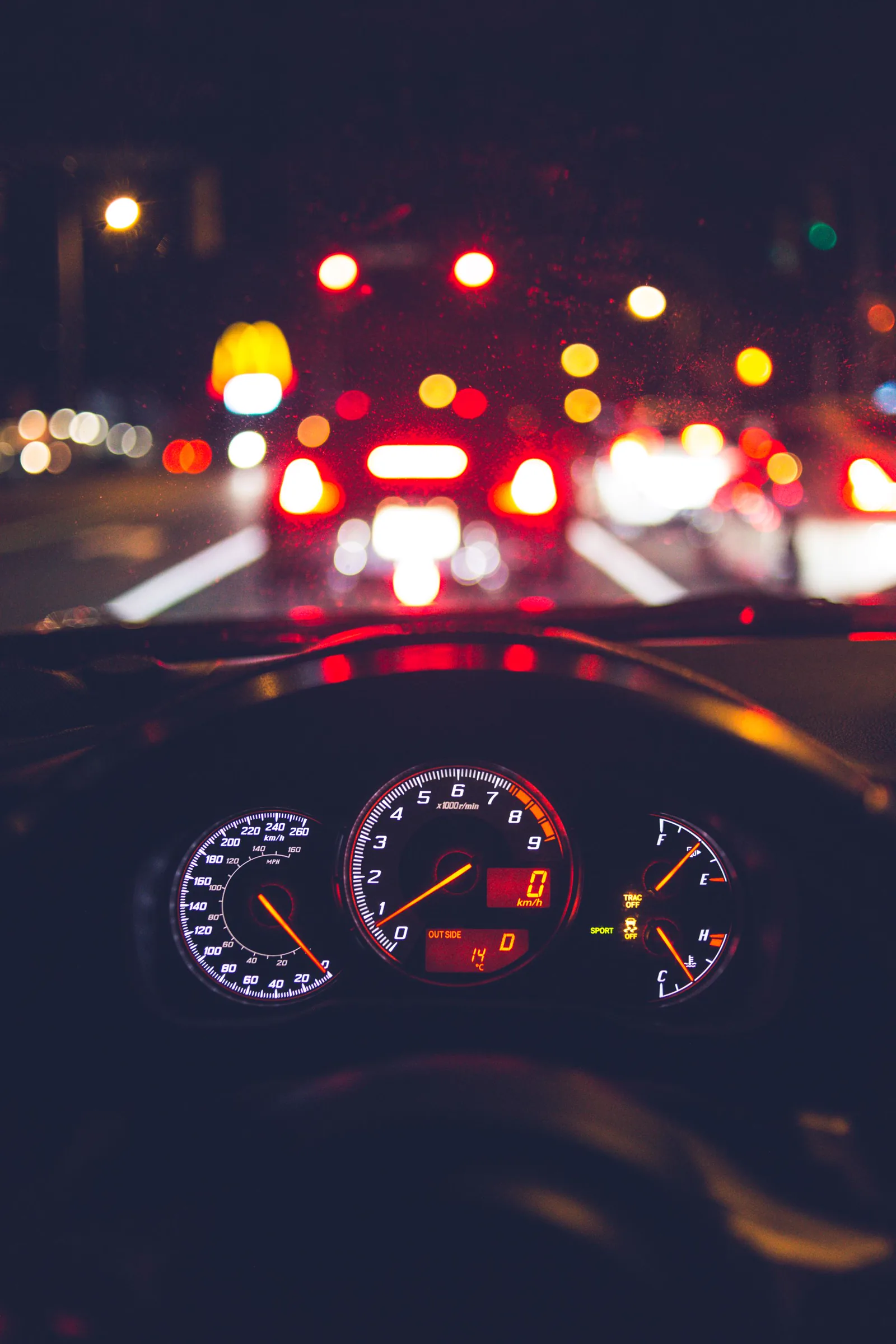 Vista do motorista à noite, com o trânsito desfocado pelo para-brisa e o velocímetro aceso